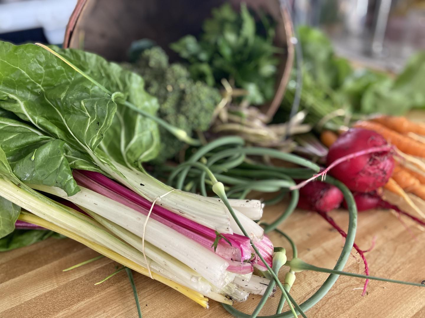 Bunch of chard on a wooden surface with vegetables in the background