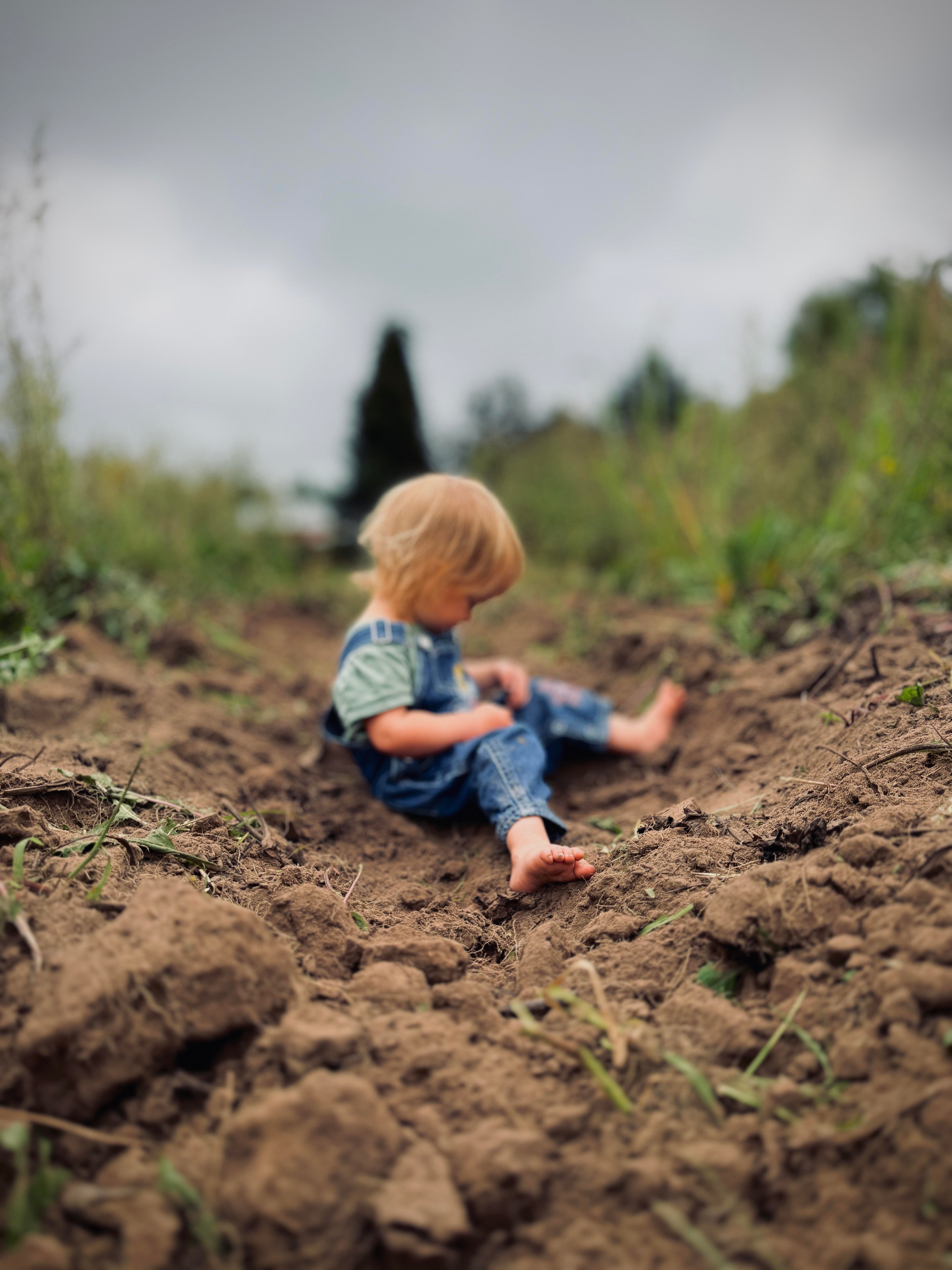 Child sitting in a field of mud on a cloudy day