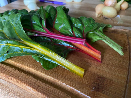 Colorful swiss chard leaves on a wooden cutting board with onions in the background